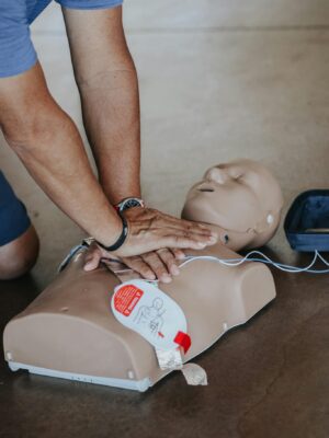 Hands demonstrating CPR technique on a training mannequin with AED.