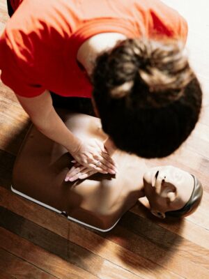 Instructor performs CPR on mannequin during training session on wooden floor.