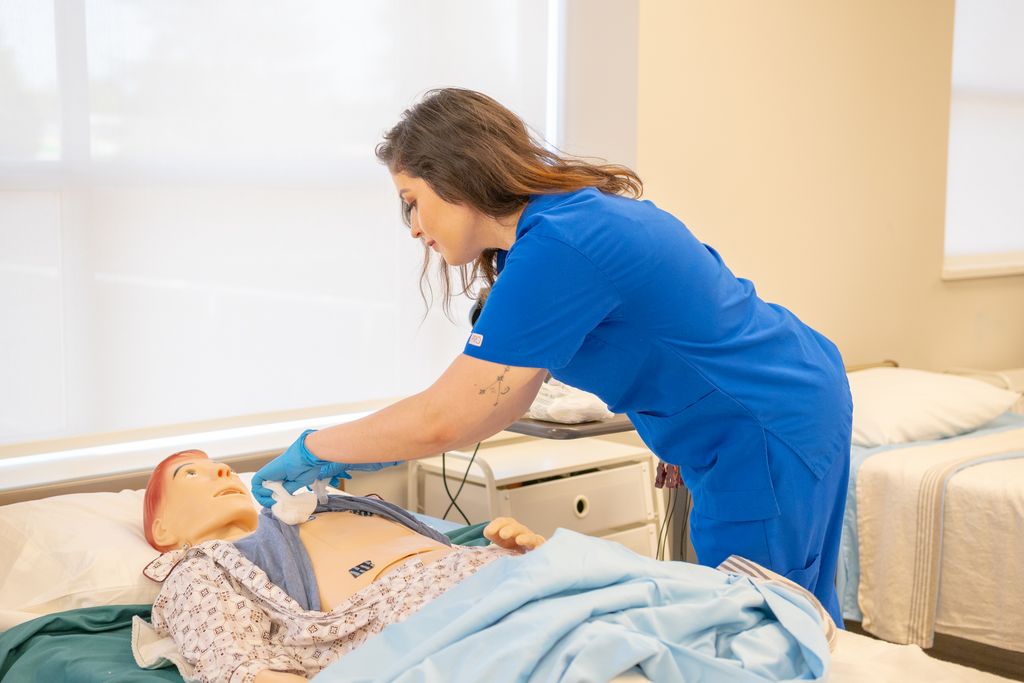 A nurse in blue scrubs trains on a medical dummy in a healthcare facility.